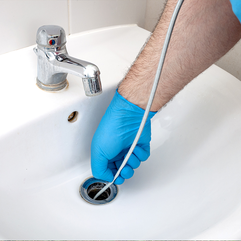 plumber unclogging a bathroom sink drain with a snake